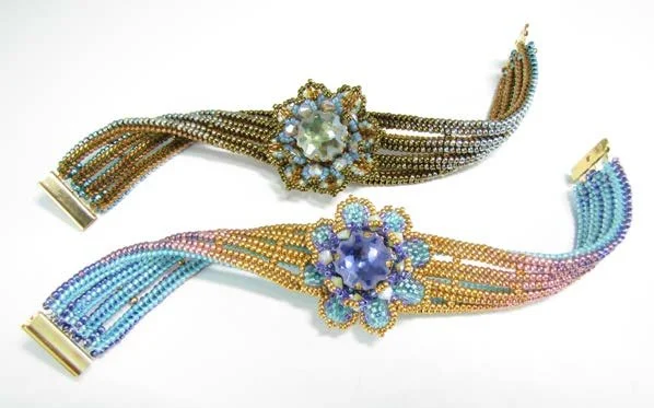 Two decorative beaded bracelets with large floral embellishments, one with yellow, blue, and purple beads and the other with blue, gold, and pink beads.