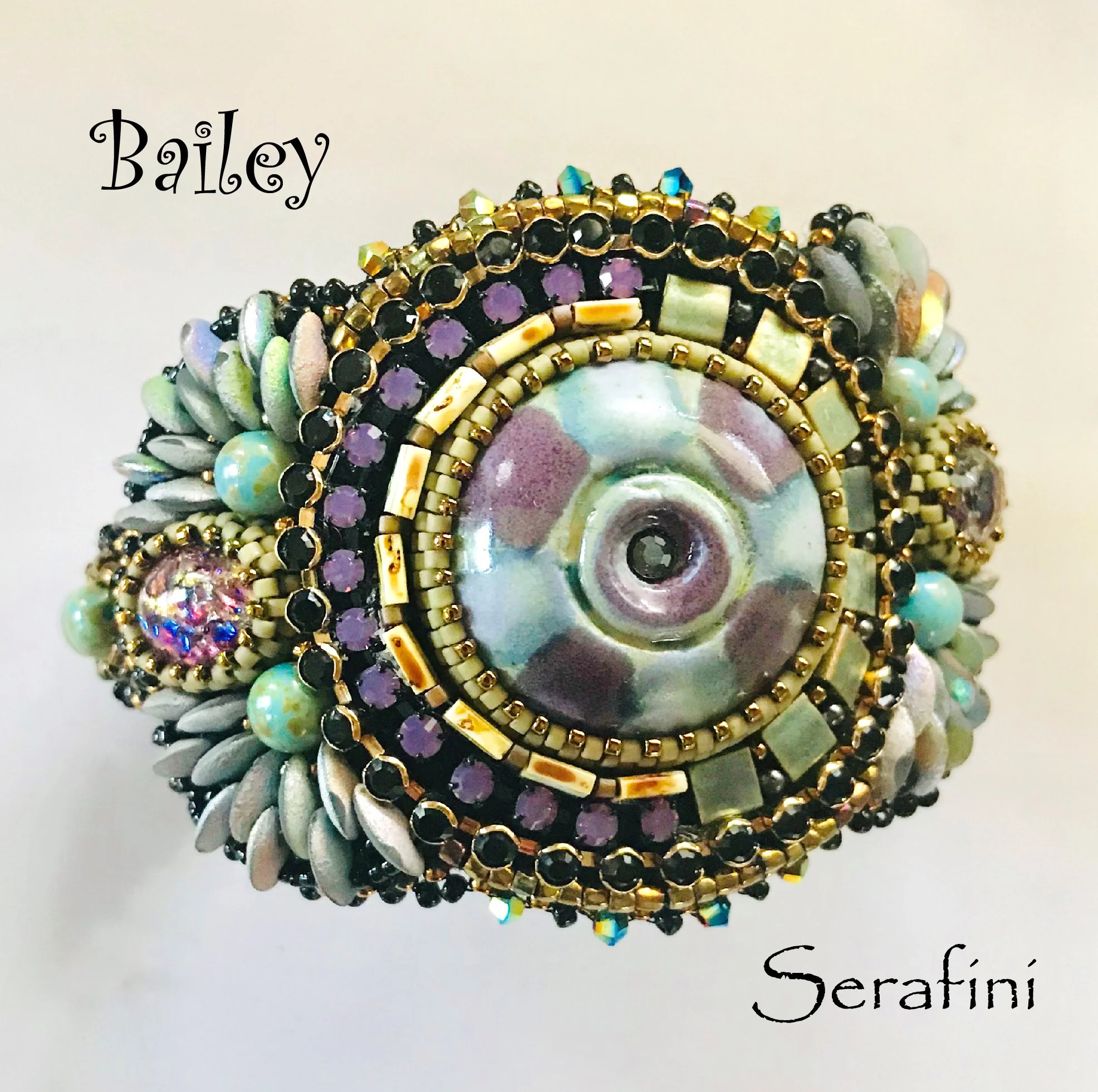 Close-up of a colorful, intricate beaded jewelry piece with various beads including black, purple, cream, and iridescent. The jewelry has swirling and layered patterns and the word 'Serafini' is written in black cursive text at the bottom.