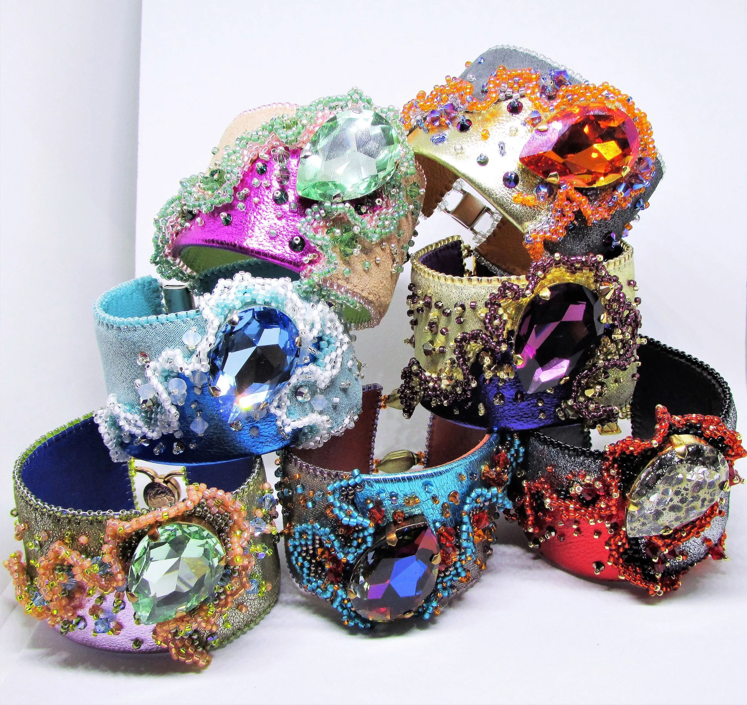 Collection of colorful, jeweled bracelets with large, faceted gemstones and intricate beadwork displayed on a white surface.