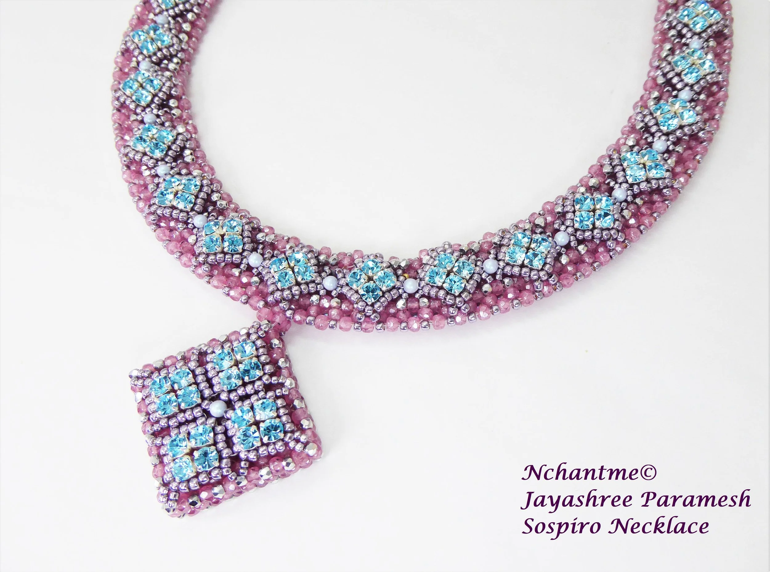 A pink beaded necklace with blue and silver rhinestones and white beads, designed as a traditional Indian jewelry piece, with a portion hanging down. Text in the bottom right corner reads: "Nchantme© Jayashree Paramesh Sospiro Necklace."
