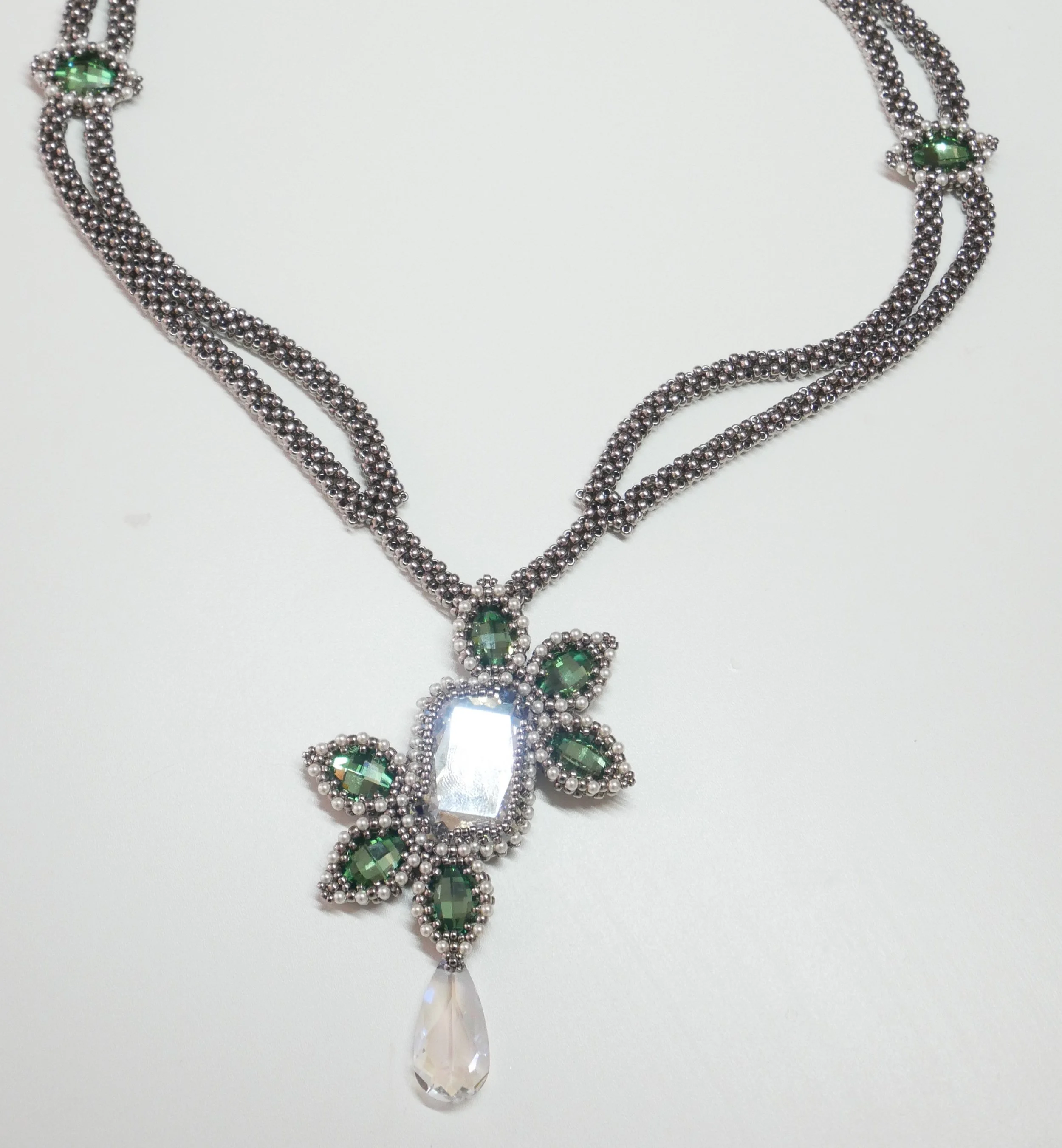Jewelry set with green gemstones and silver beads, featuring a necklace and a matching pendant with a large teardrop-shaped crystal.