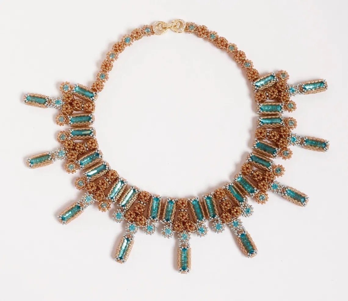 A necklace with gold beads and turquoise stones laid out on a white background.