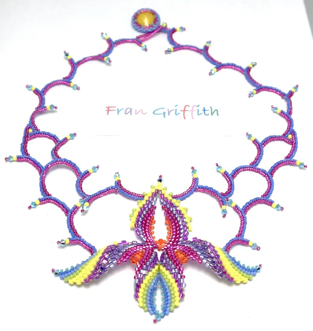 Colorful beaded necklace with a floral or butterfly design around a white card that has the name 'Fran Griffith' written in multicolored letters.