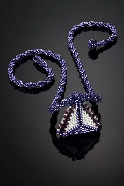 Beaded necklace with a pyramid-shaped pendant on a black reflective surface.