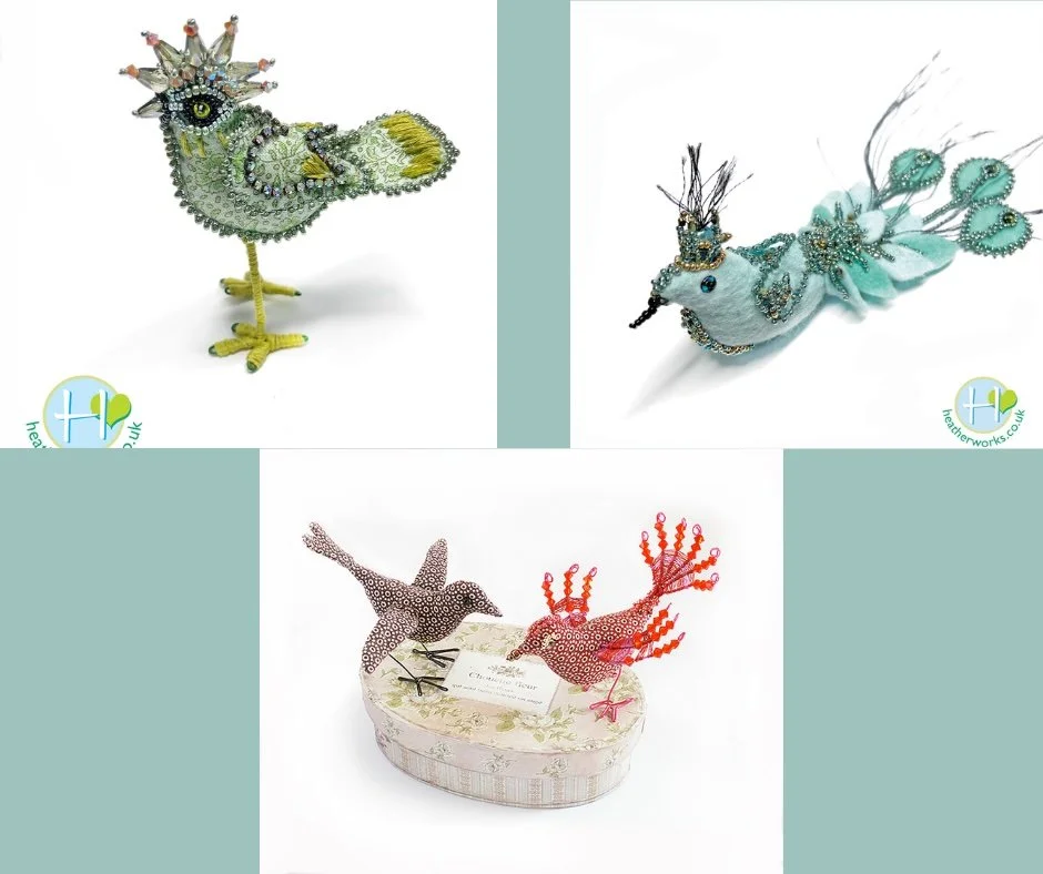Three decorative bird figurines made with beads, fabric, and wire. The top left features a green and yellow bird with a crown-like crest, the top right shows a white bird with a blue crown and tail feathers, and the bottom center has two birds, one b