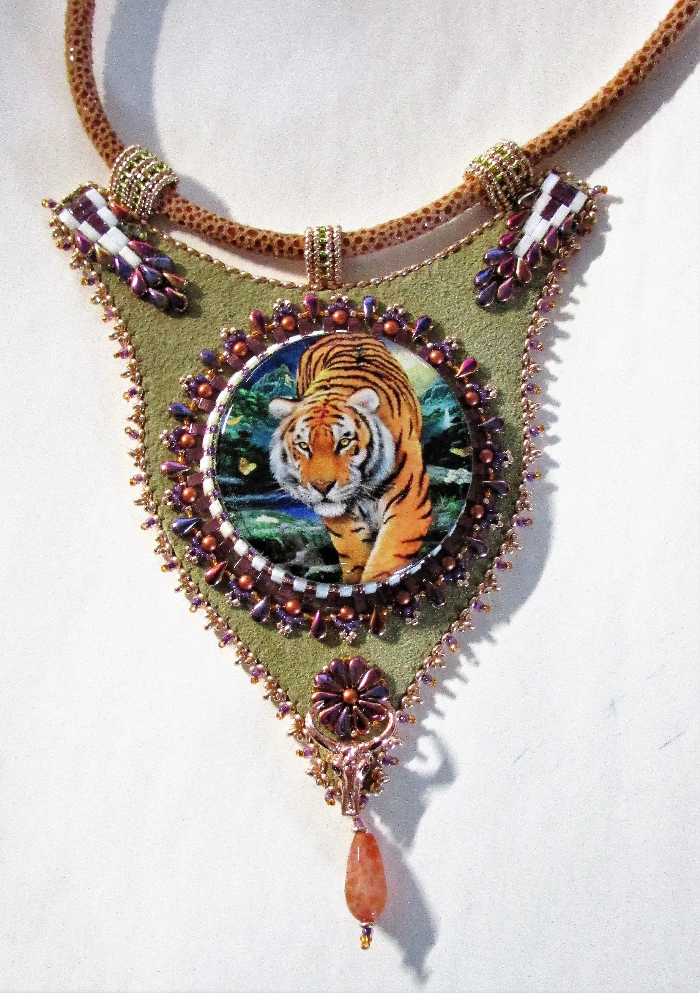 A necklace featuring a tiger image at its center, surrounded by beads and ornate details, with a dangling pendant at the bottom.