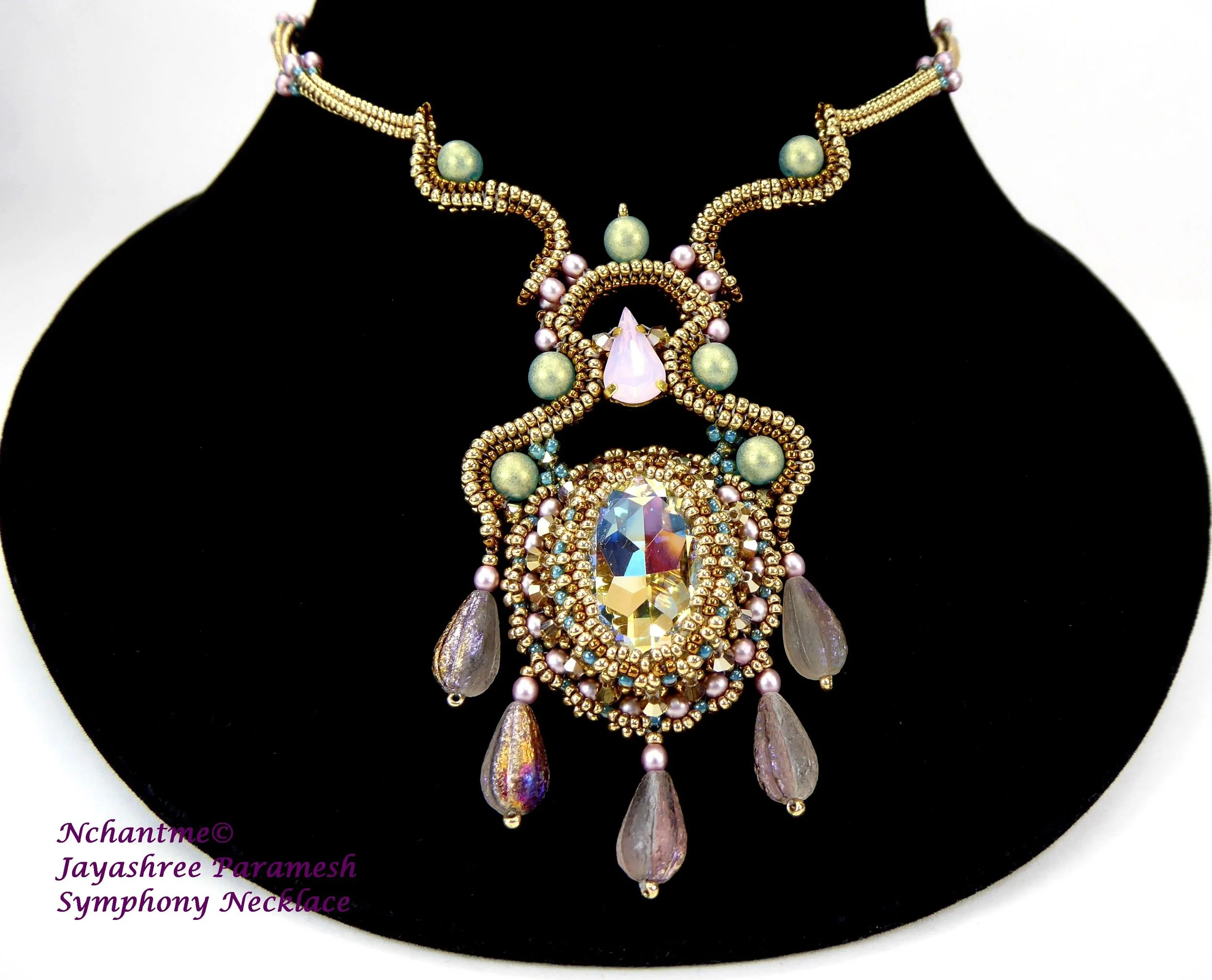 A statement necklace jewelry piece with intricate design including large clear and pink gemstones, purple teardrop-shaped beads, smaller pink and blue beads, and gold-tone accents, displayed on a black background.