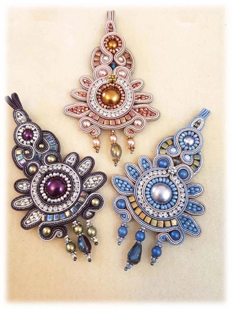 Three elaborate pendant necklaces with intricate designs and various colored beads and stones, displayed on a plain background.