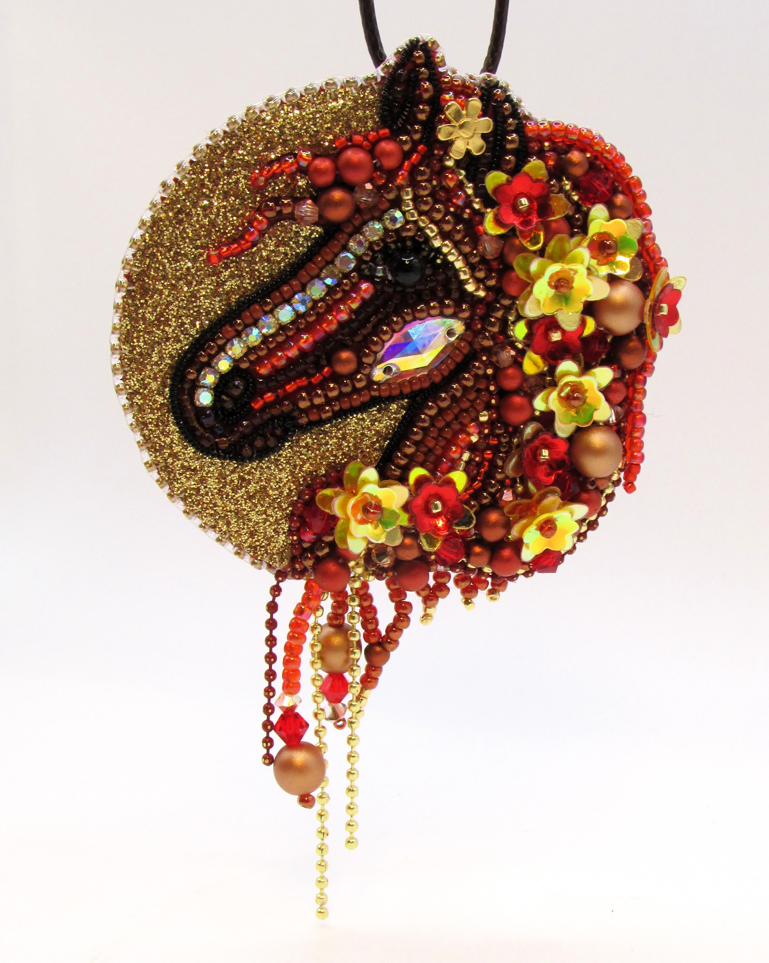 A decorative pendant designed to resemble a ladybug, adorned with numerous beads, rhinestones, and small flower embellishments in shades of red, gold, and black, hanging from a black cord.