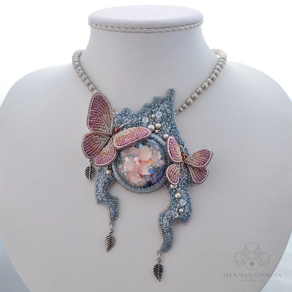 An ornate beaded necklace with butterfly and leaf charms displayed on a white bust.