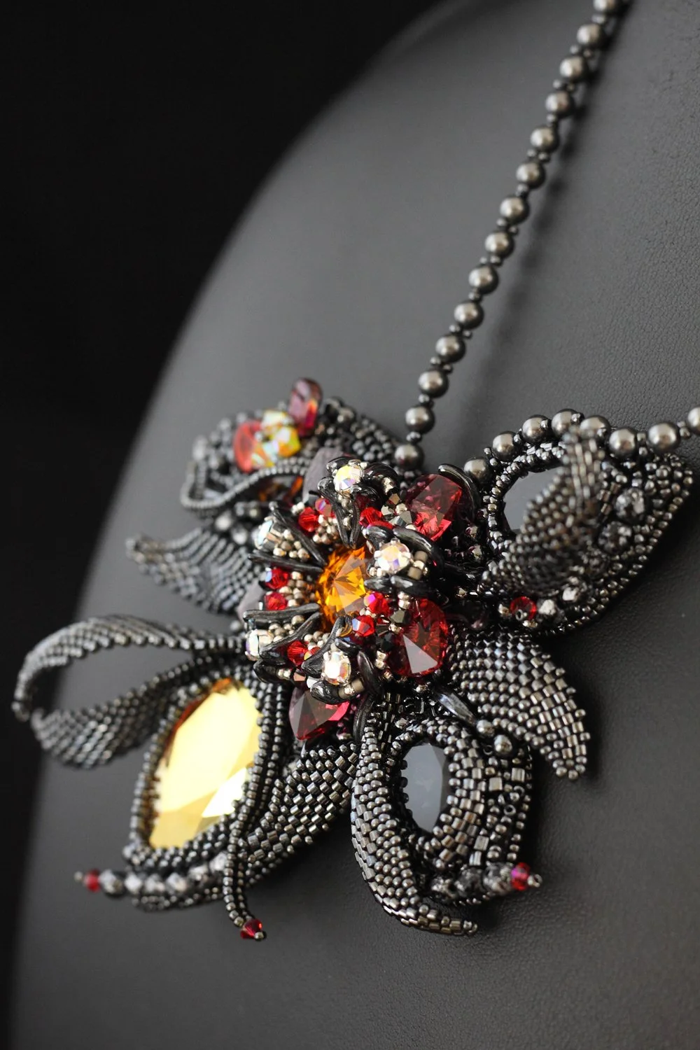 Black beaded butterfly necklace with red, orange, yellow, and clear gemstones, displayed on a black surface.