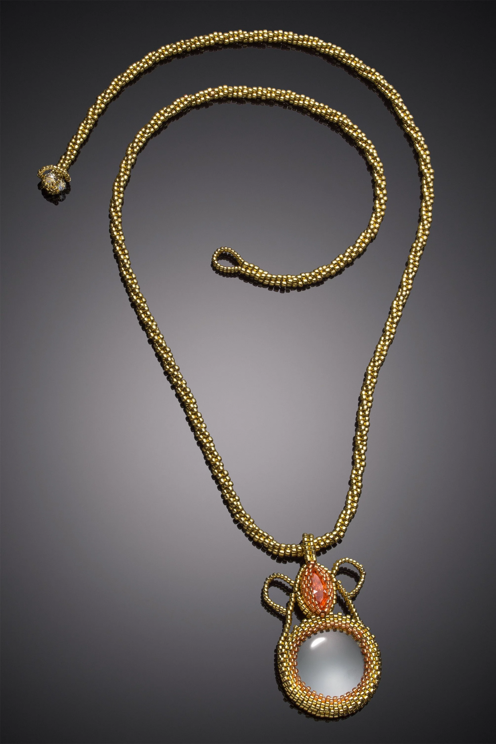 Gold necklace with a large oval orange gemstone pendant, elaborate gold wire surrounding, and a white spherical bead at the bottom