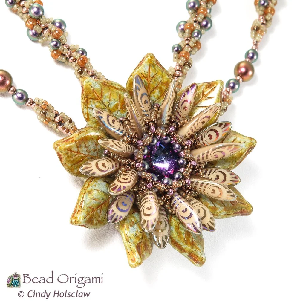 A beaded necklace with a large flower-shaped pendant that has multicolored beads, leaf-shaped charms, and a purple gemstone at the center. The necklace features multicolored pearls in pastel shades.