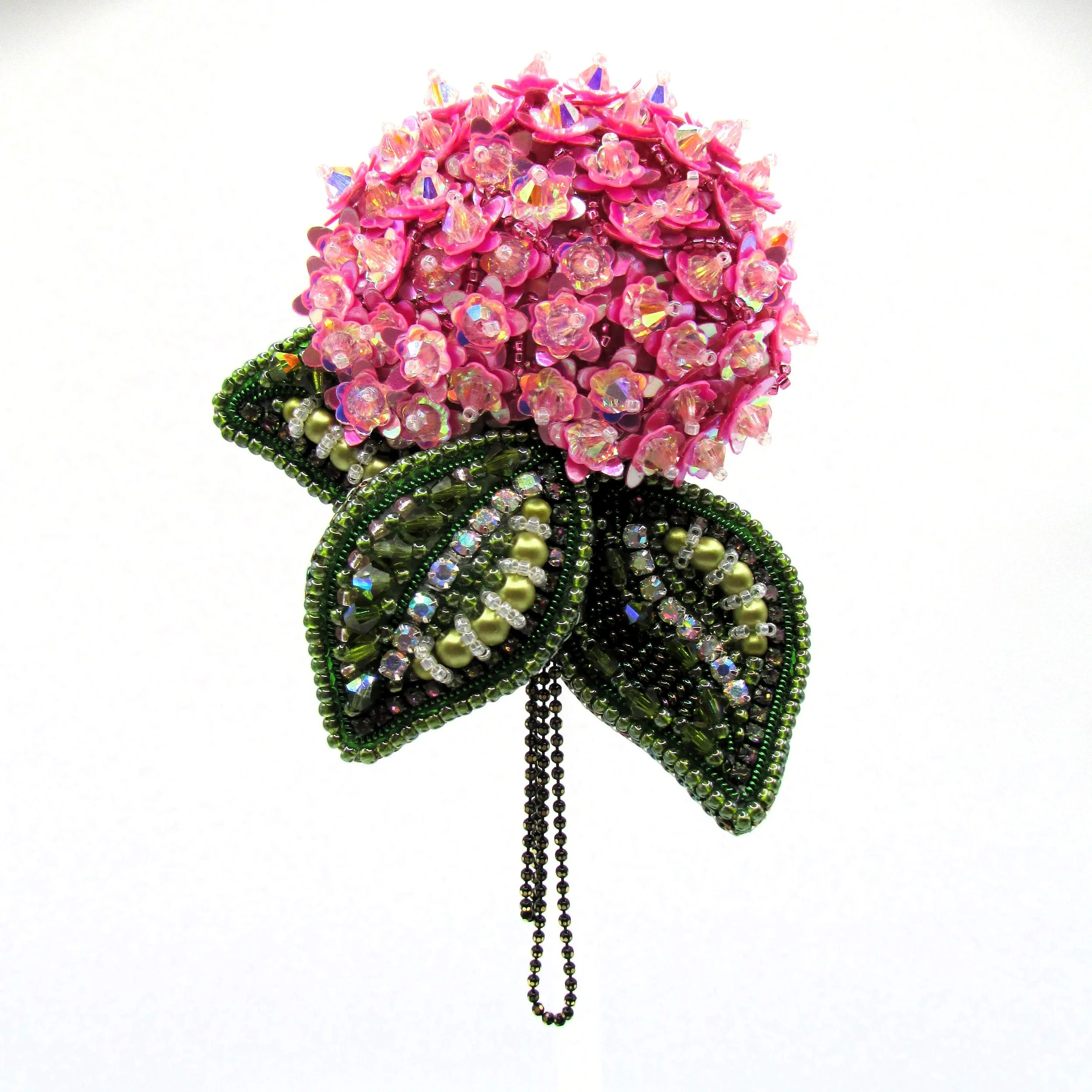 A decorative flower made of pink and iridescent beads with green bead leaves and strings hanging below, displayed against a white background.