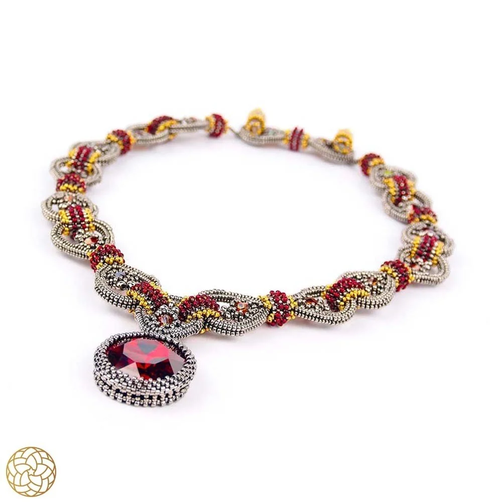 A necklace with intricate silver, red, and yellow beadwork and a large red gemstone pendant.