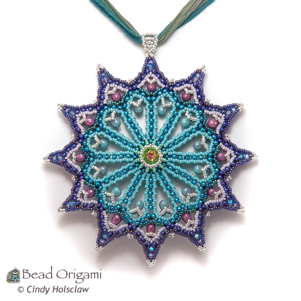 A beaded necklace with a large star-shaped pendant featuring a detailed, colorful bead design resembling a mandala or flower, attached to a multi-strand fabric necklace.