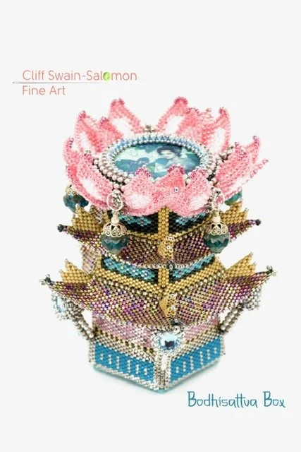 Decorative box adorned with intricate beadwork, featuring a Buddha image in the center, pink lotus petals on top, and hanging earrings, with text indicating it is a fine art piece by Cliff Swain-Salomon.