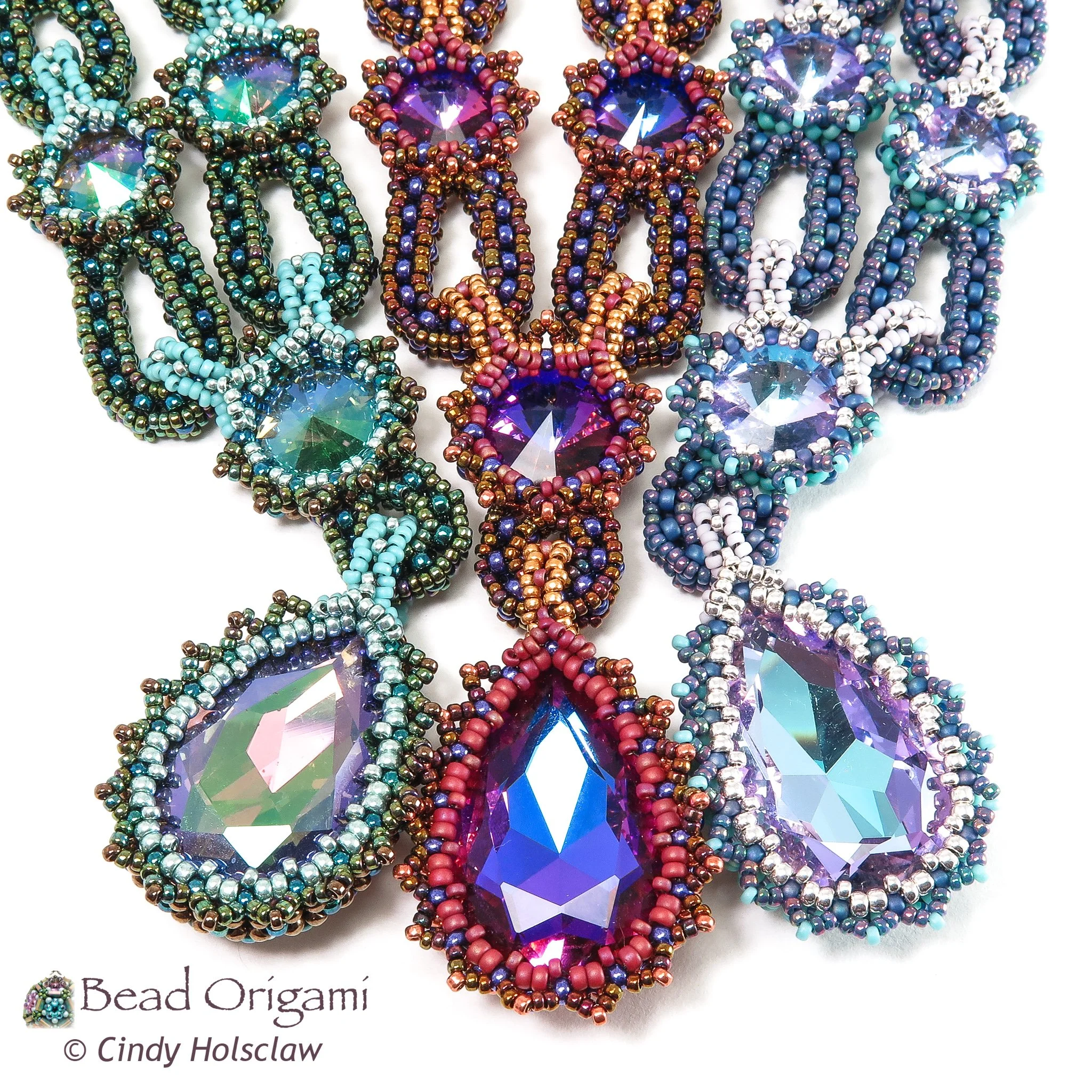 Close-up of beaded jewelry with large, faceted, purple, teardrop-shaped beads surrounded by smaller beads in blue, purple, silver, and copper colors, arranged on a white background.