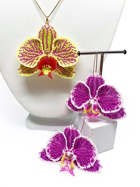 Colorful beaded butterfly jewelry, including a necklace and two brooches, displayed on a white stand.