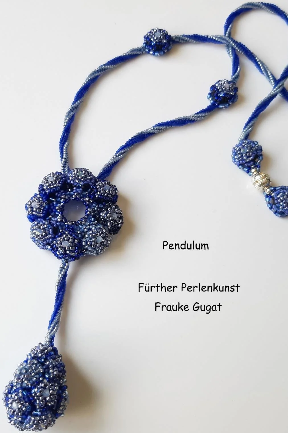 Blue and silver beaded jewelry with a circular pendant and several beaded balls, labeled as Pendulum, created by Frauke Gugat from Fürther Perlenkunst.