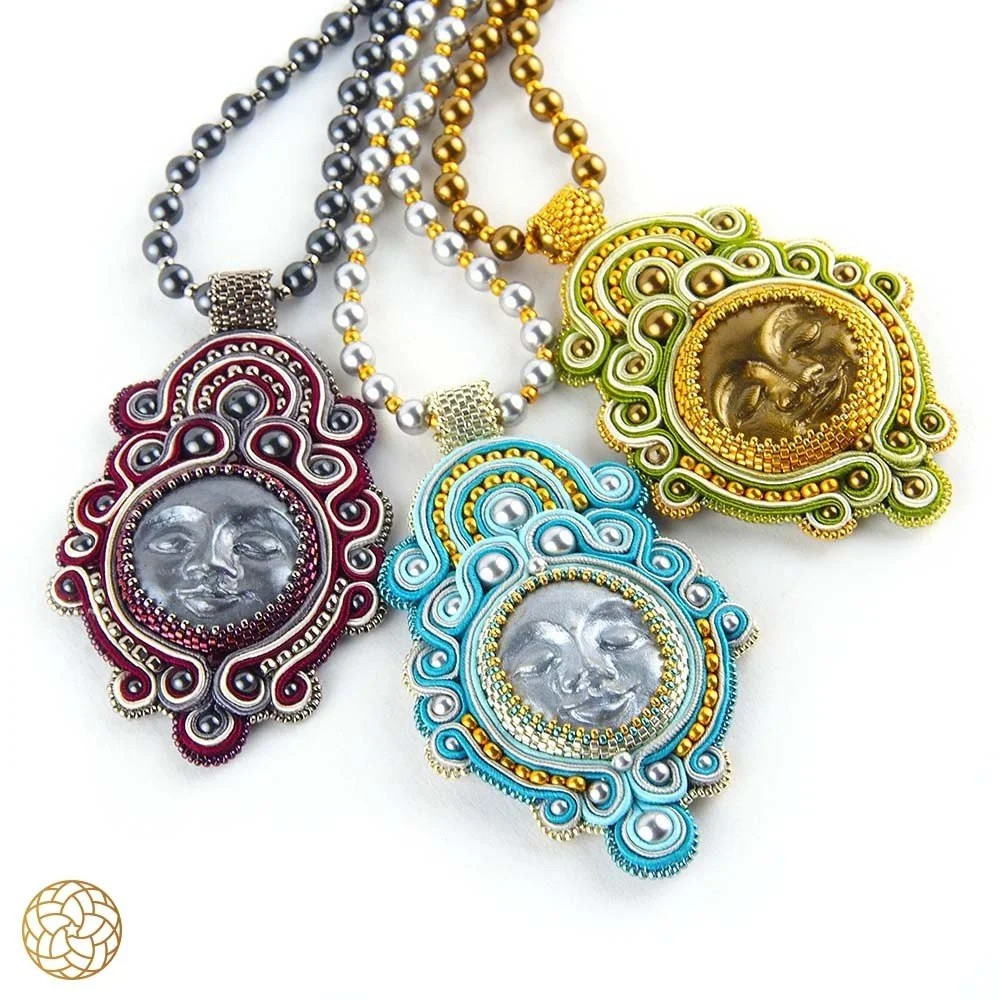 Three colorful pendant necklaces with intricate designs, featuring a metallic face at the center, in red, yellow-green, and blue colors.