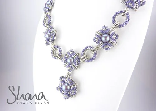 Elegant necklace with purple and silver beads and large pearl-like pendants displayed on a white bust.