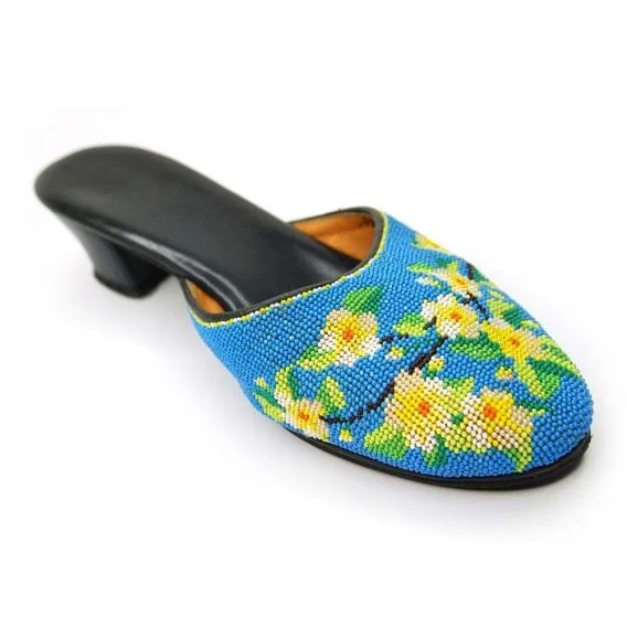 A decorative shoe with a black heel and a bright blue upper covered in yellow and white floral beadwork.