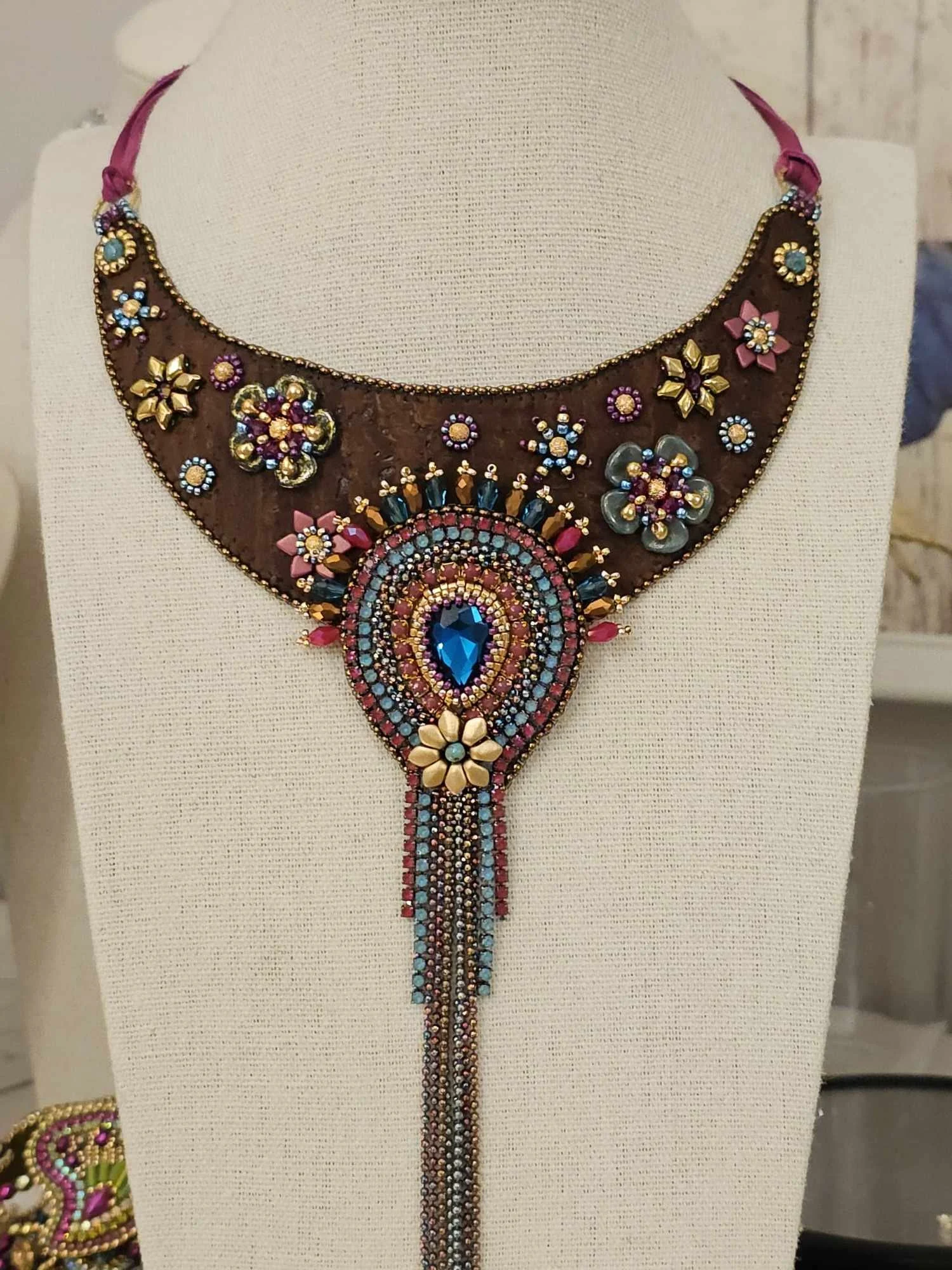 A colorful, ornate beaded necklace with floral and circular patterns displayed on a mannequin bust.