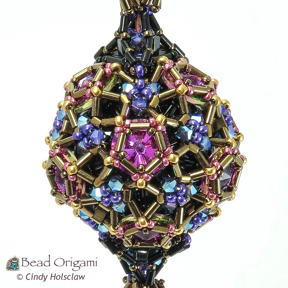 Colorful beaded geometric ornament with pink, purple, blue, and gold beads, titled 'Bead Origami' by Cindy Holsclaw.