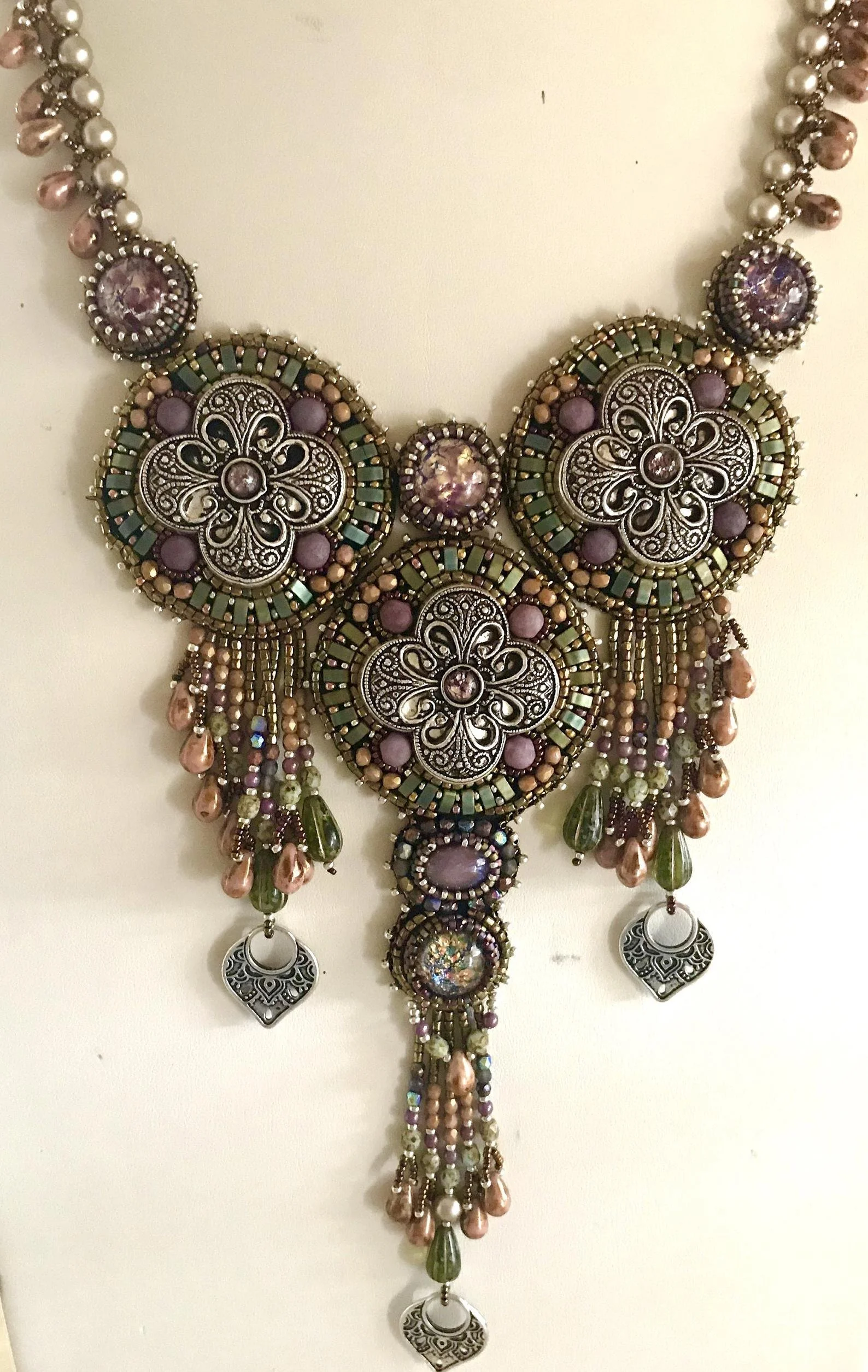 A multi-strand necklace with intricate silver filigree, purple, pink, and green beads, and dangling pendants.