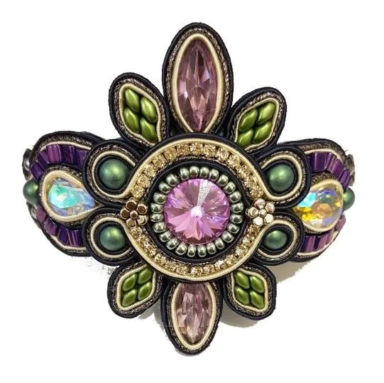 A decorative brooch featuring various colored gemstones, including pink, green, purple, and iridescent stones, arranged in a floral and circular pattern.