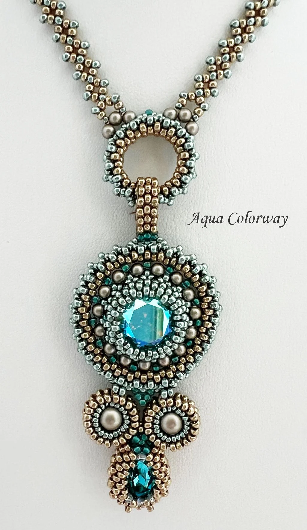 A detailed beaded necklace with a circular pendant featuring a large blue gem, smaller pearls, and beads in metallic and teal colors. The necklace design is intricate and ornate.