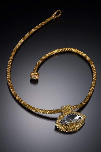 Gold necklace with a large teardrop-shaped gemstone pendant on a black background.