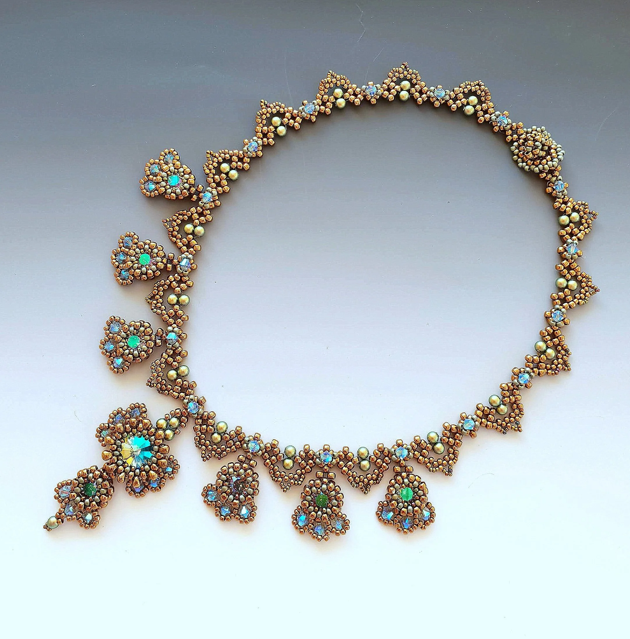 Close-up of a beaded jewelry necklace with intricate floral and leaf designs, featuring shiny beads in gold and pearl colors with iridescent accents.