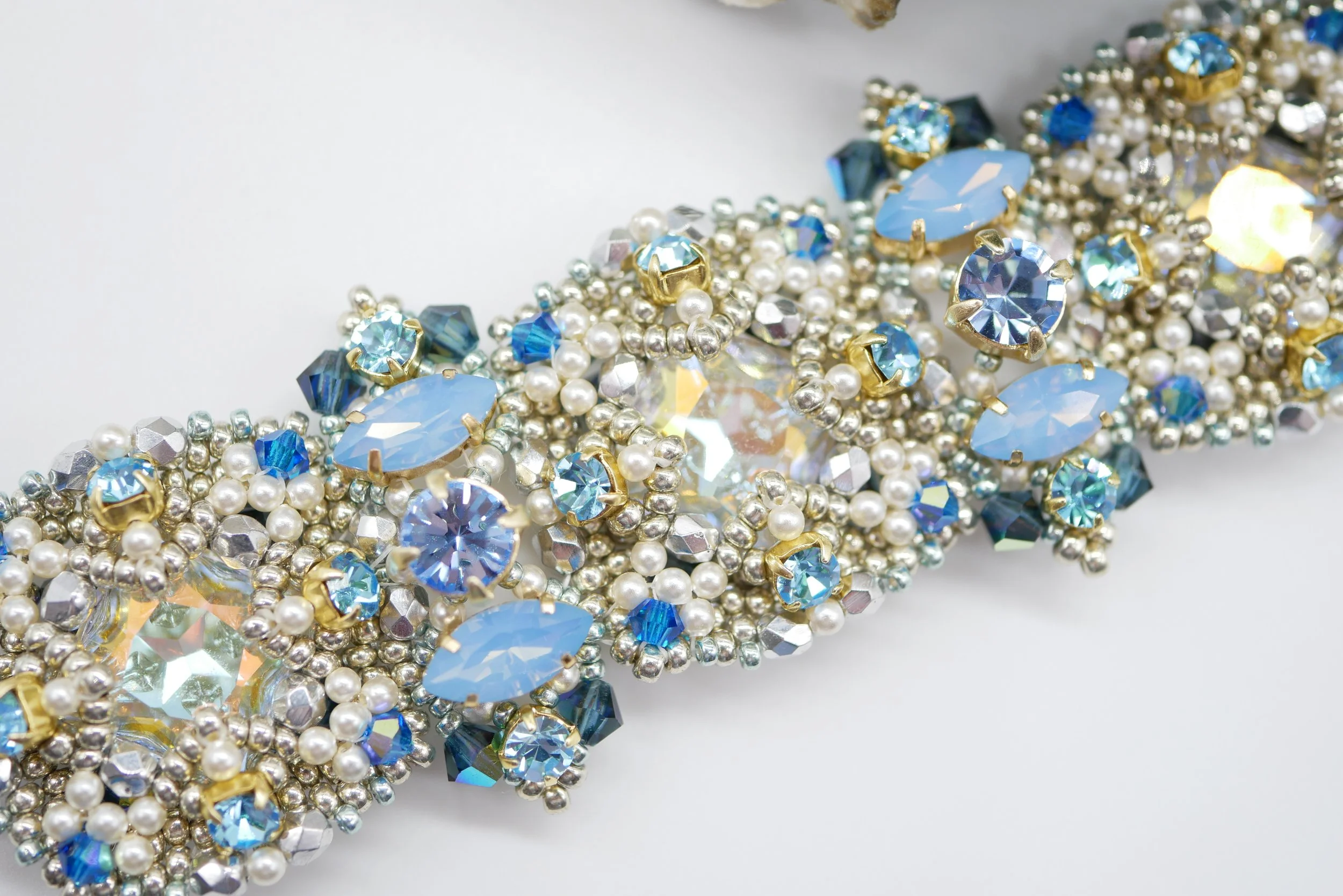 Close-up of assorted beads and rhinestones in blue, white, and silver with gold settings, arranged in a decorative pattern.