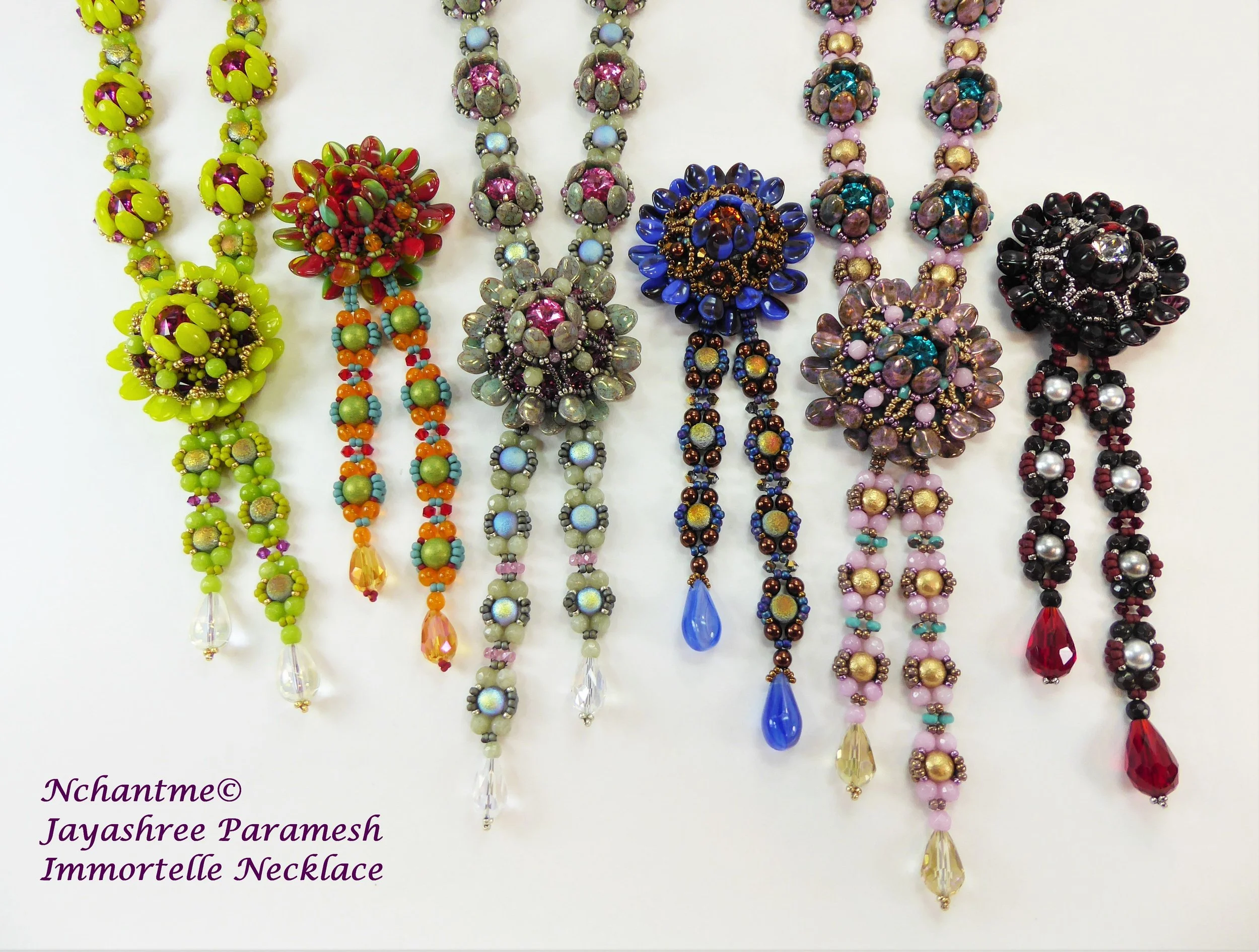 Colorful bead necklaces displayed in a row with intricate designs and large gemstone-like pendant drops, arranged vertically.