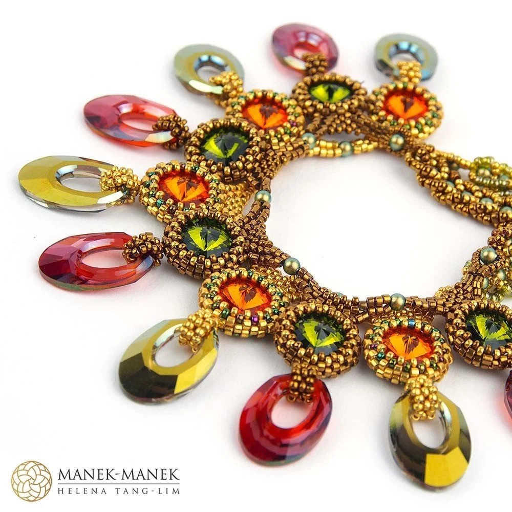 Close-up of an intricate colorful beaded necklace with orange, green, and yellow gemstones, hanging on a white background.