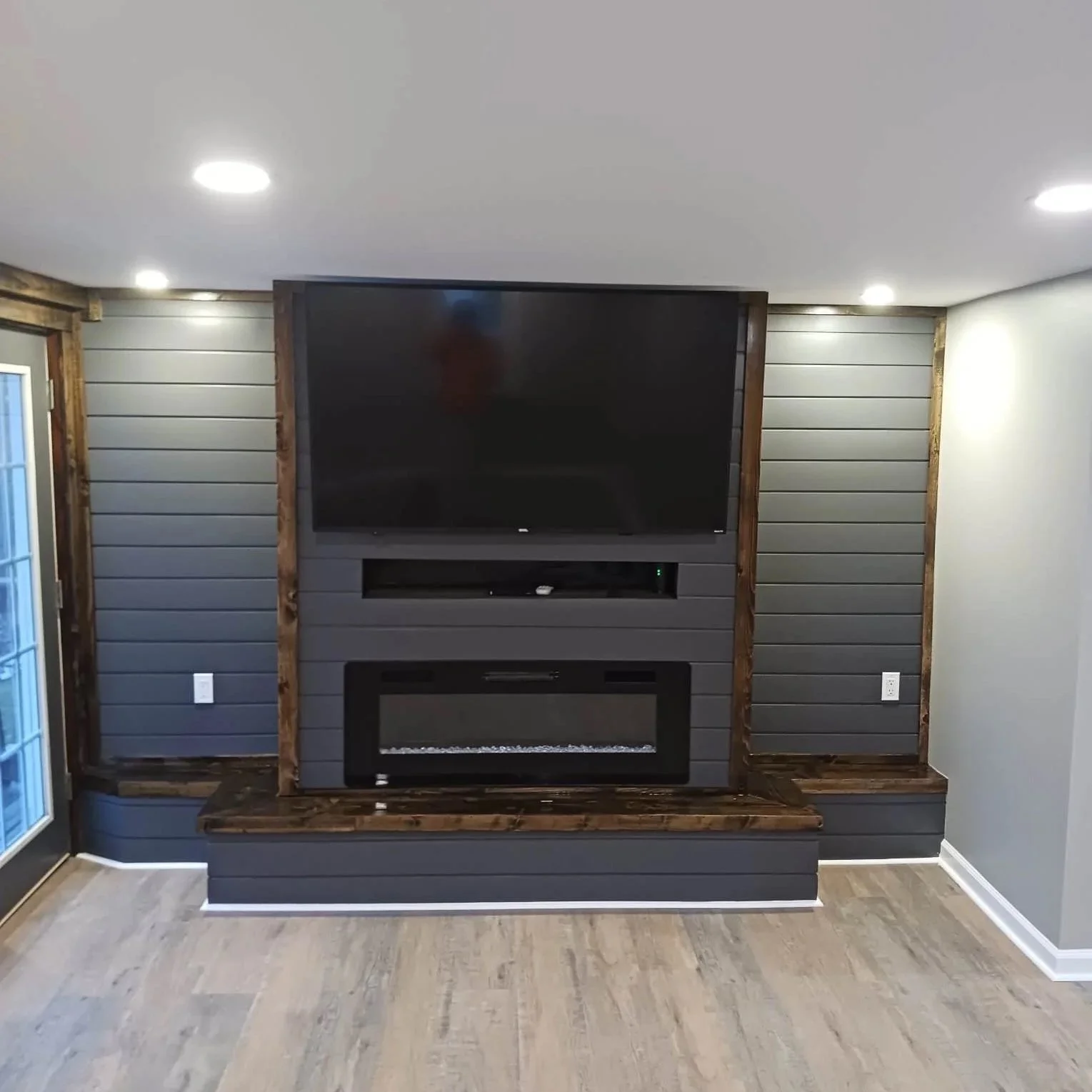 Living room entertainment wall with a large flat-screen TV, shiplap paneling, and a modern electric fireplace at the base.