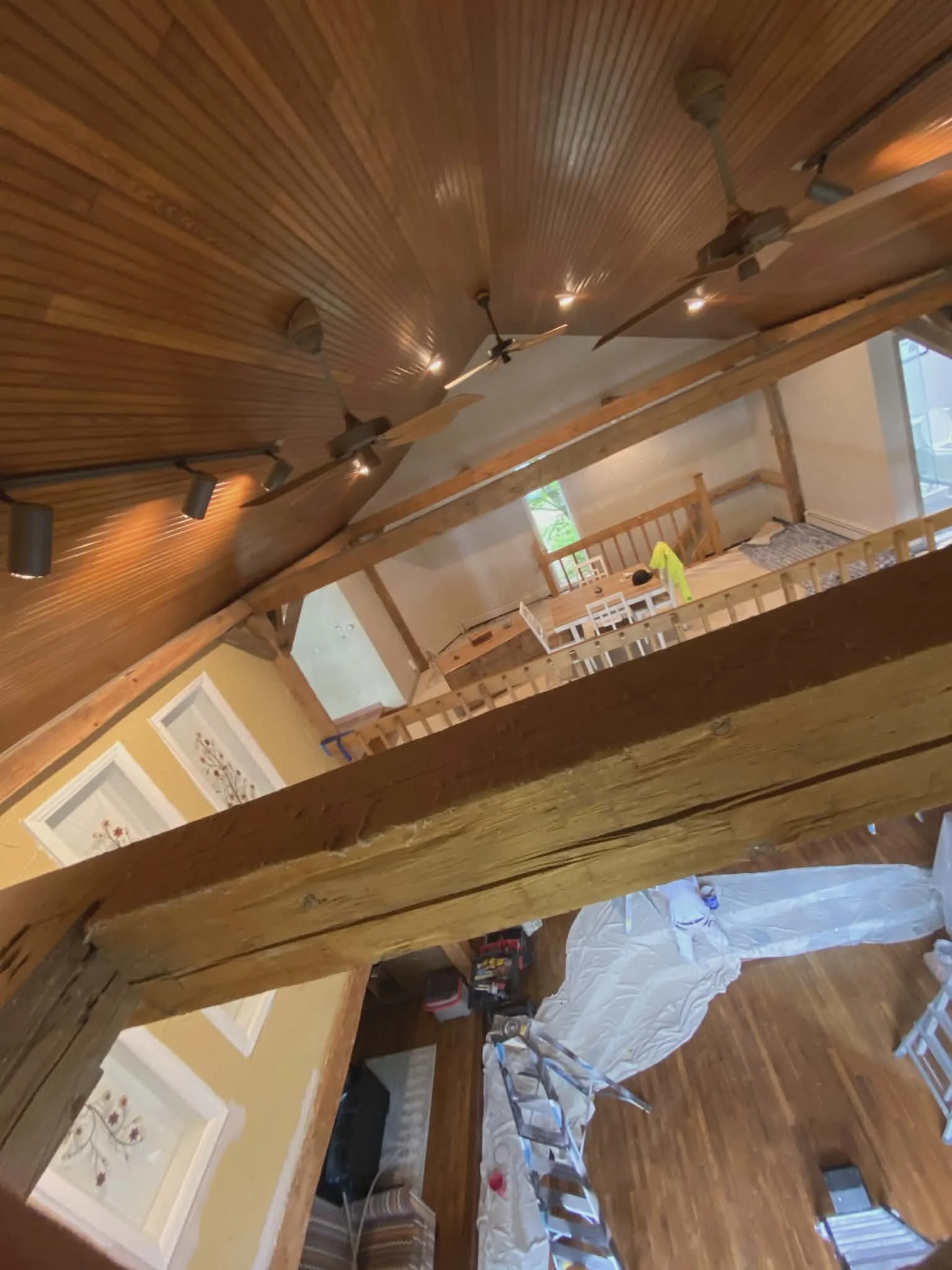 Interior of a house under renovation, showing wooden ceiling and beams, track lighting, a ceiling fan, and construction materials in the living space.