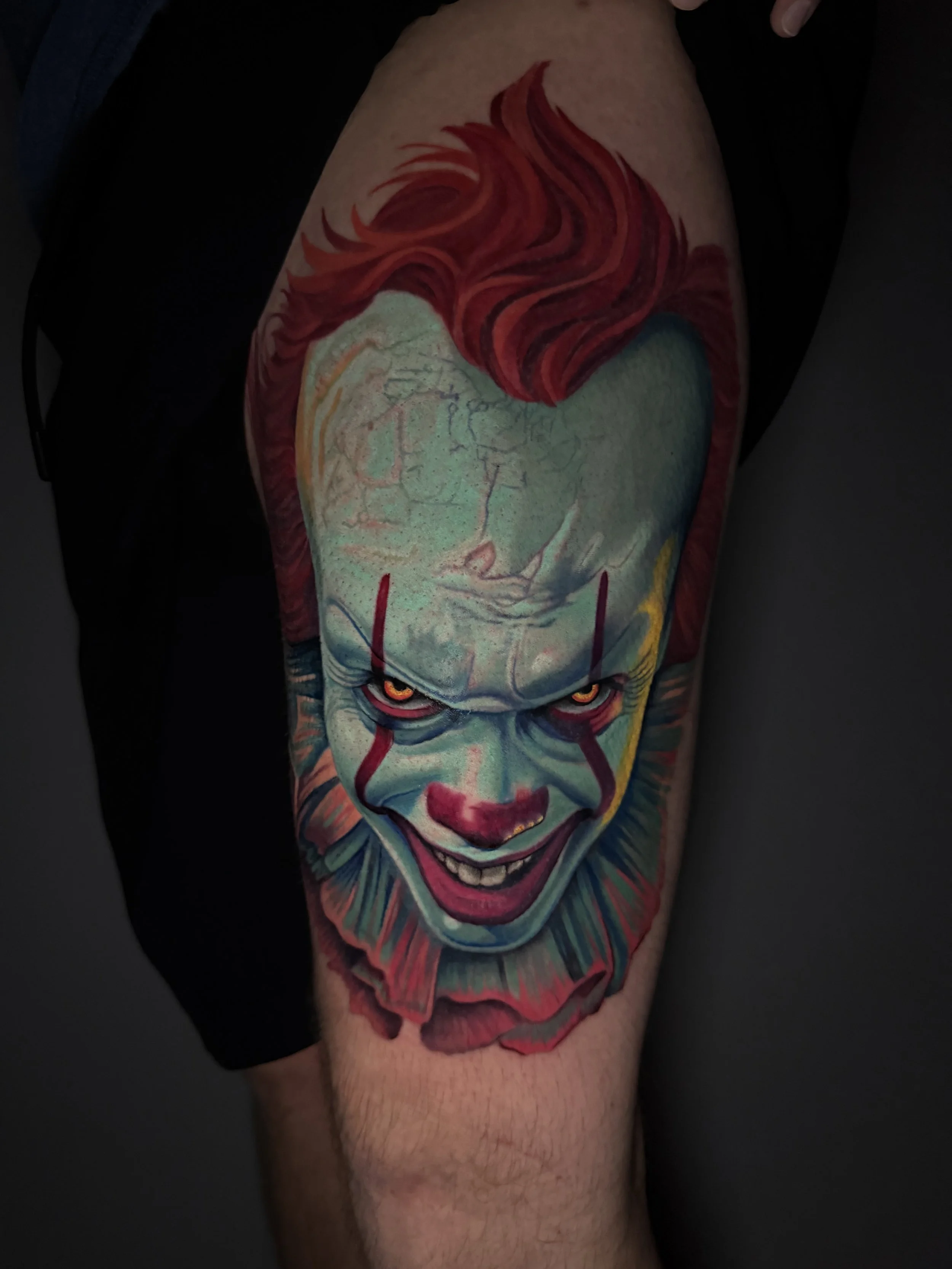 Colorful tattoo of Pennywise the Dancing Clown from It, with red hair, yellow eyes, and a sinister smile on a person's thigh.