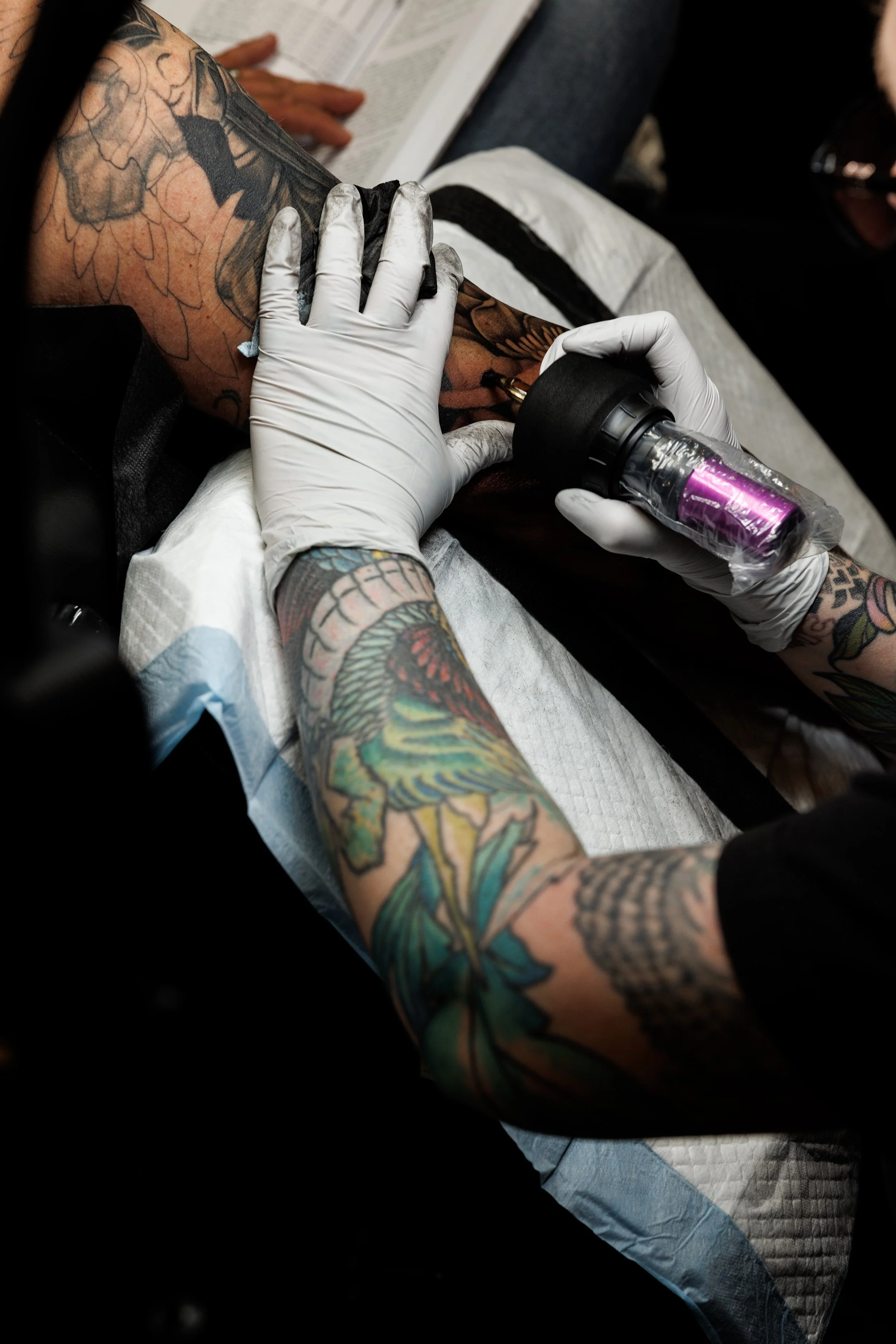 Tattoo artist in gloves working on a client's arm with a tattoo machine.