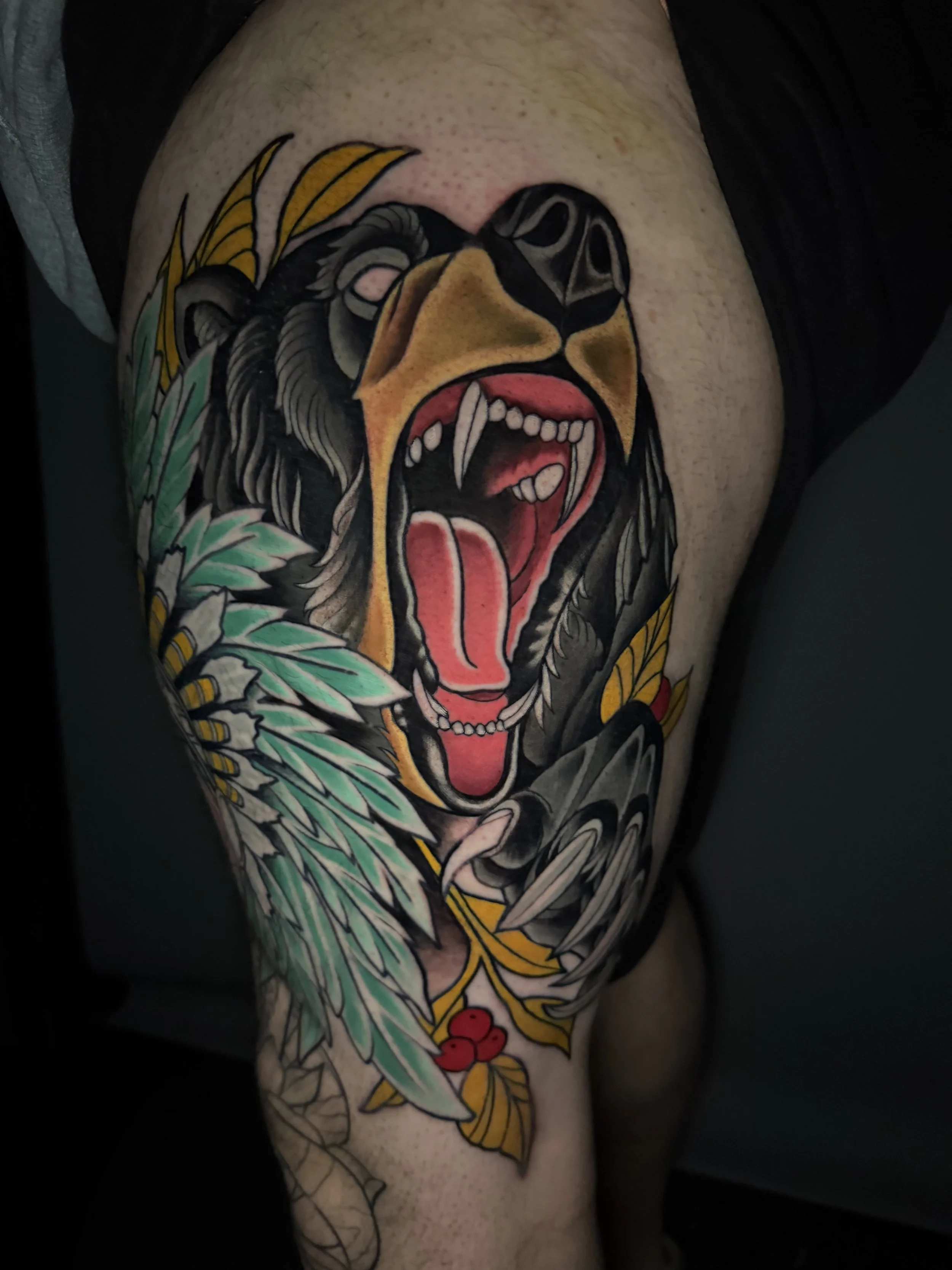 Tattoo of a roaring bear with an open mouth, surrounded by leaves and small red berries.