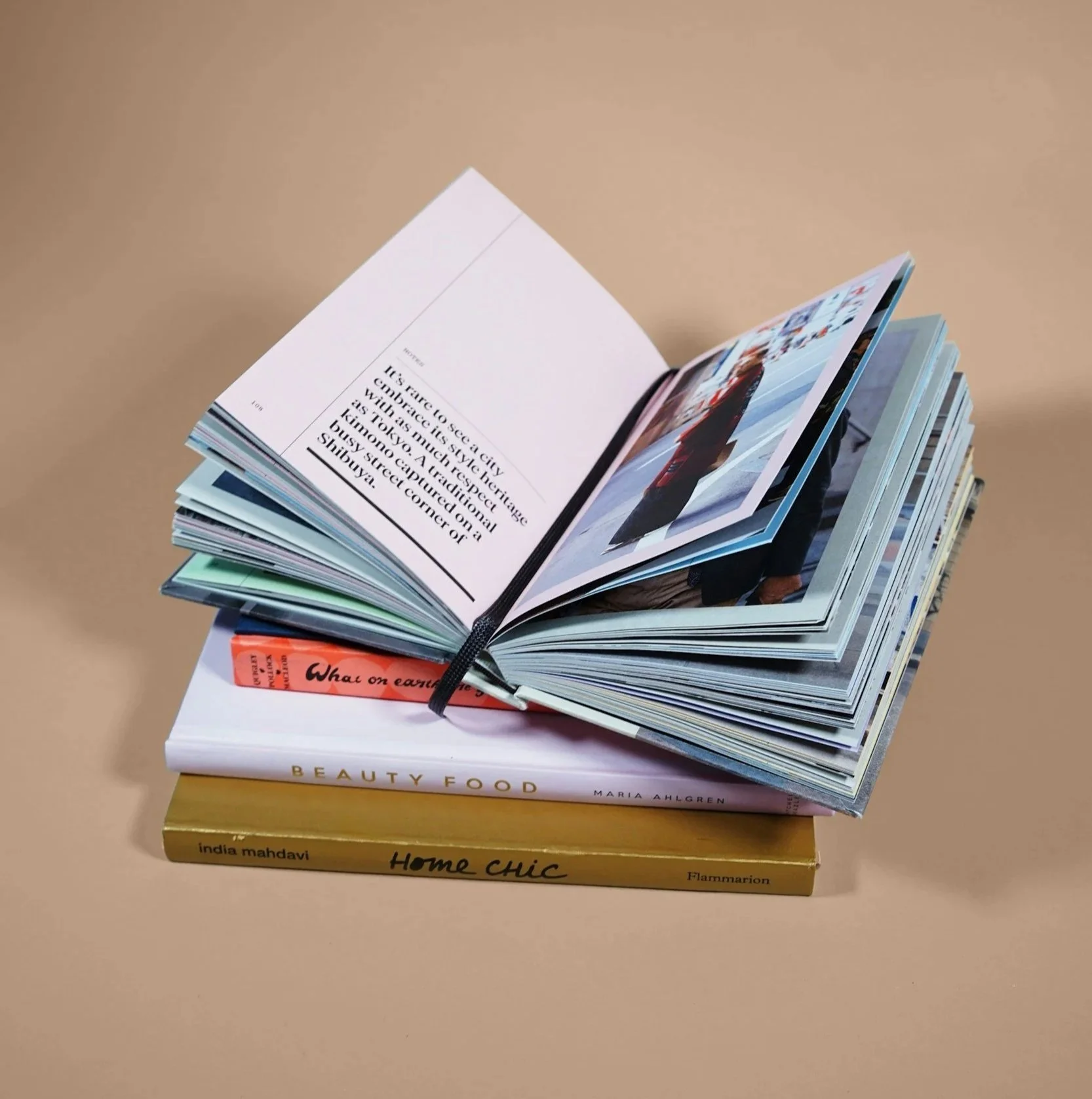 A stack of beautifully designed books with a photo book open on top. The open book shows a photograph on the right page and text on the left, arranged in a visually interesting way.