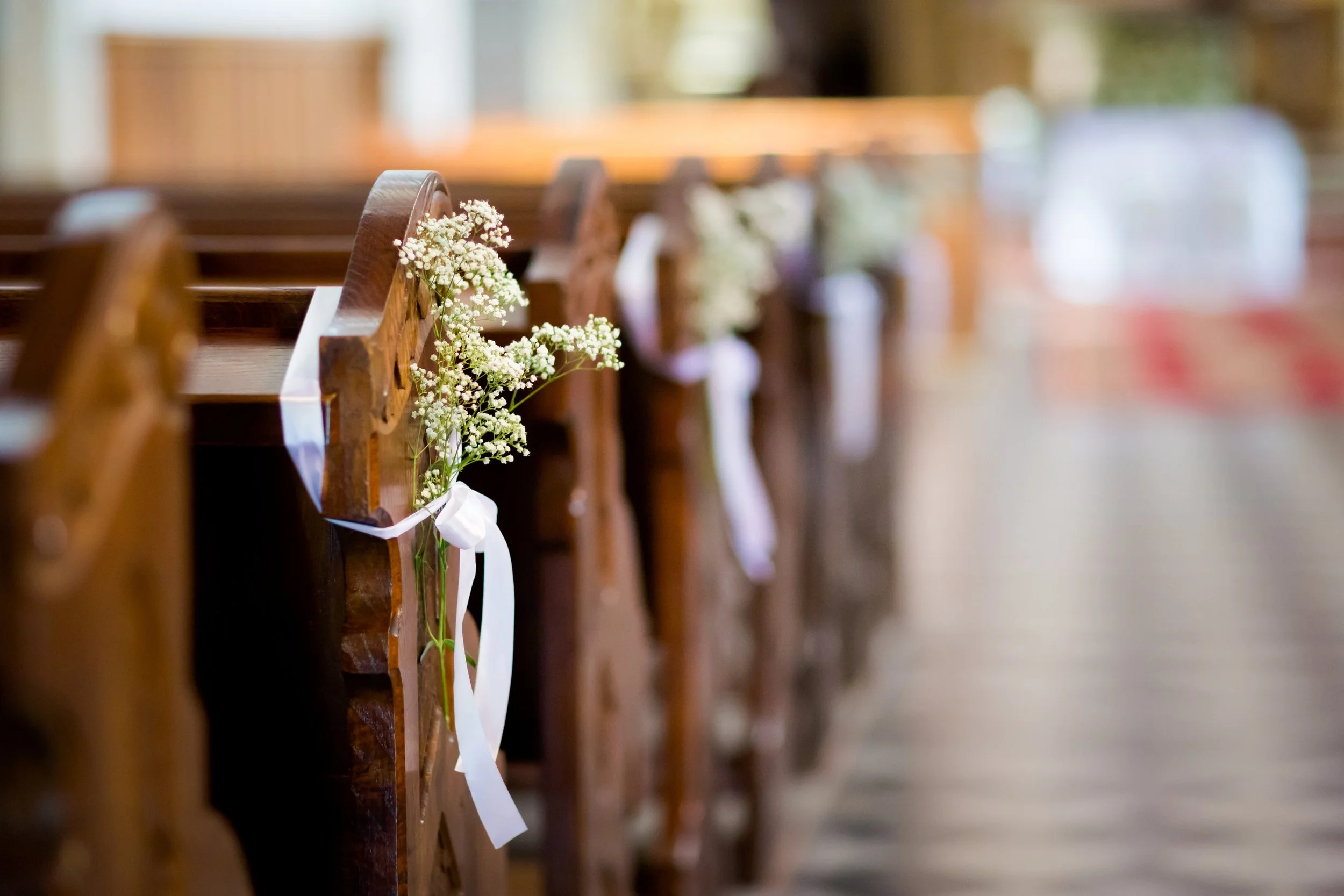 Detail von Kirchenbänken, an denen kleine weiße Blumengestecke angebracht sind.