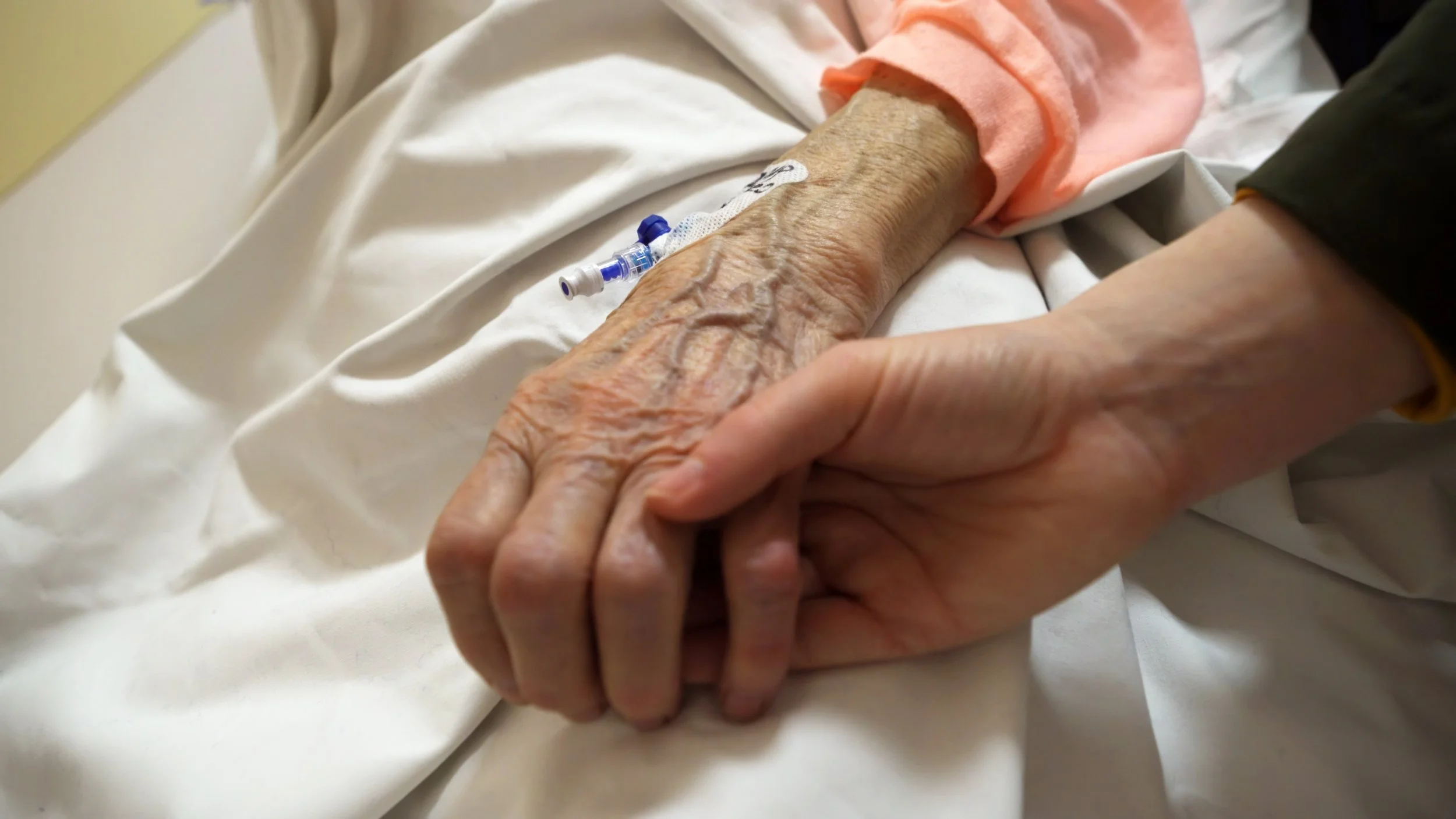 Eine jüngere Hand hält eine alte Hand mit sichtbaren Venen und einer Infusionsnadel.