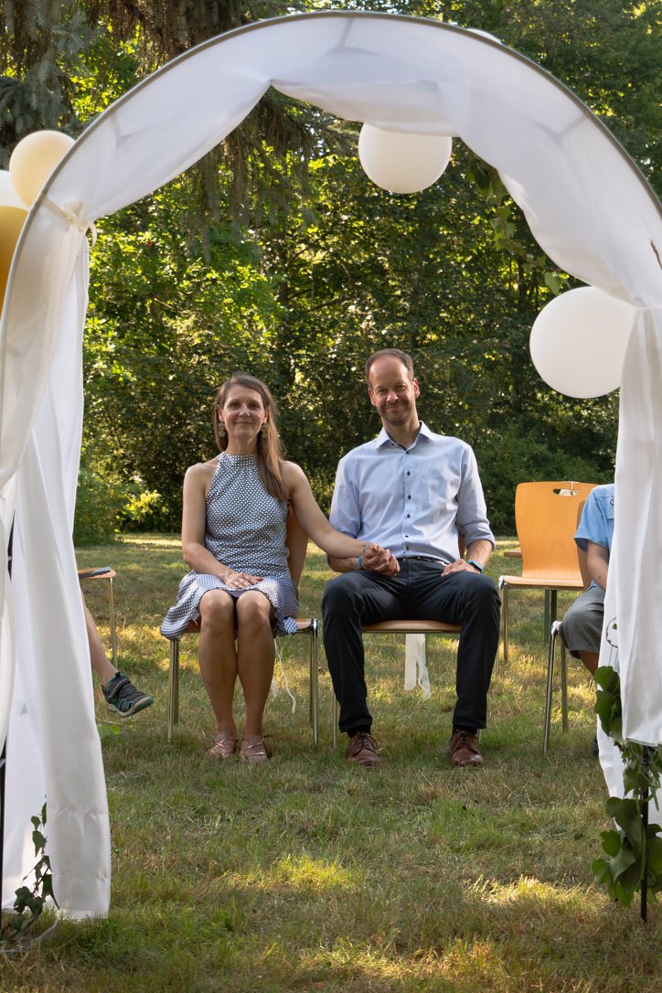 Ein Hochzeitspaar sitzt draußen. Sie halten ihre Hände und lächeln.