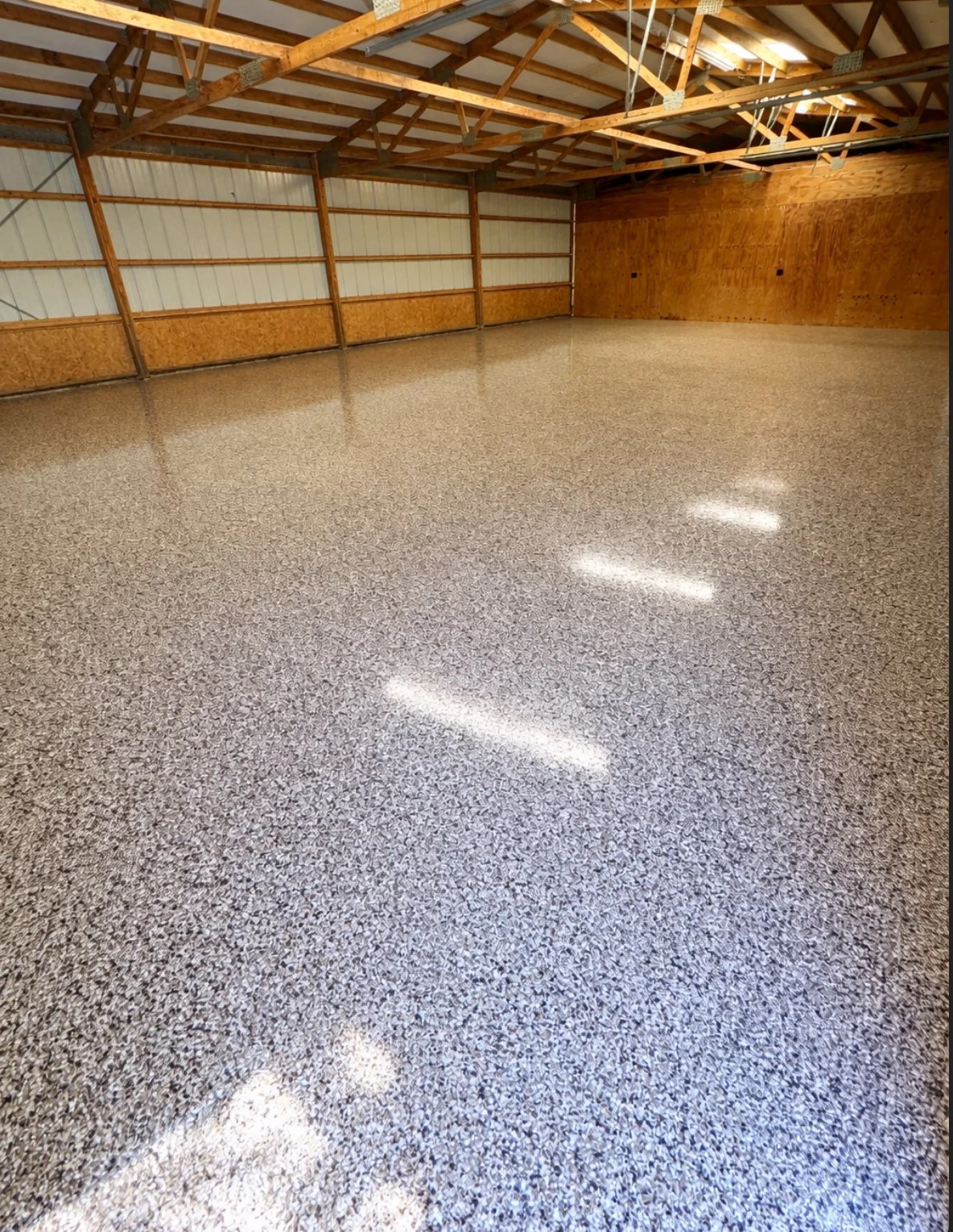 Empty indoor workshop space with polished speckled epoxy flooring, wooden walls, and exposed ceiling beams.