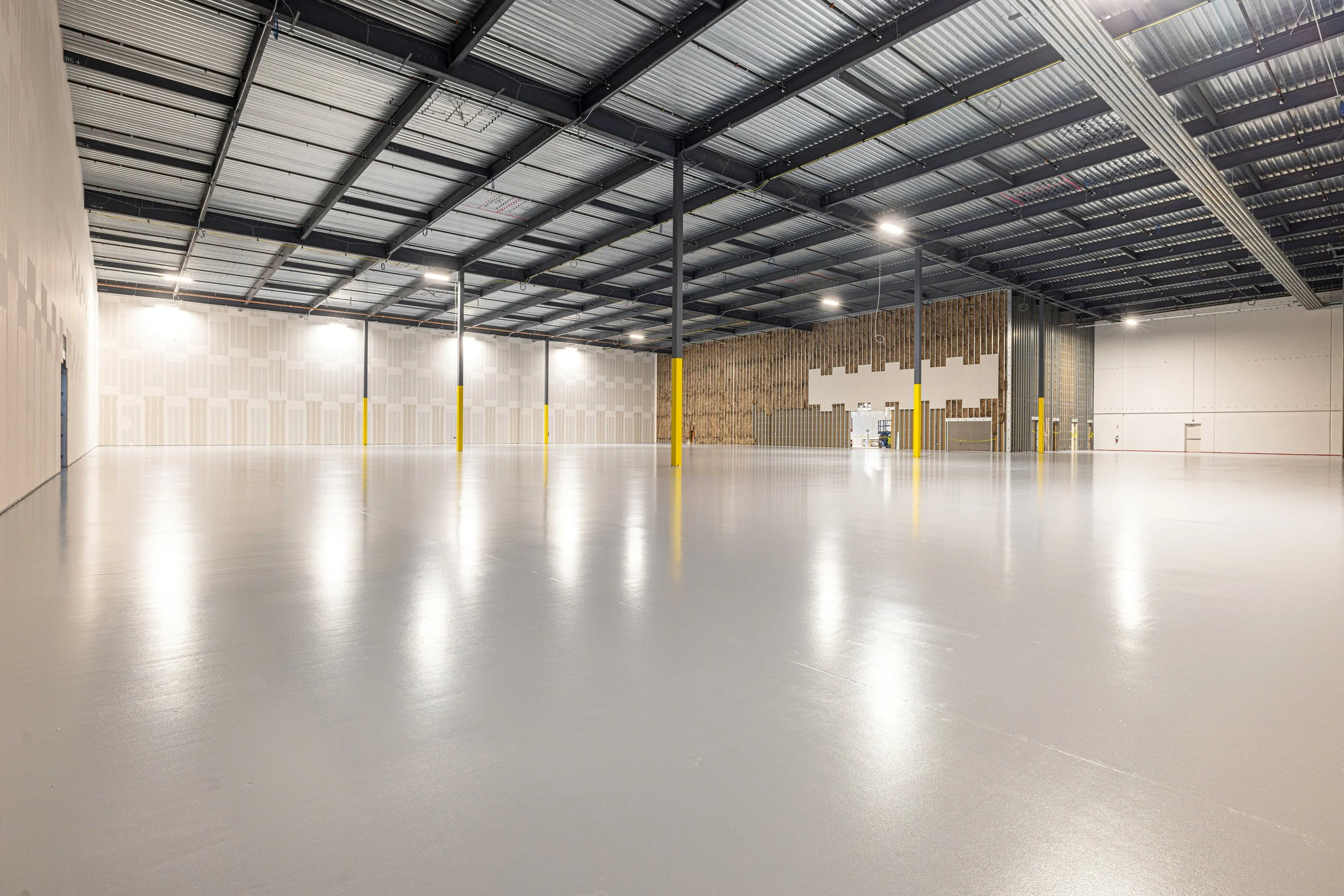 Empty commercial warehouse with epoxy floor, high ceiling with metal beams, and partially finished walls.