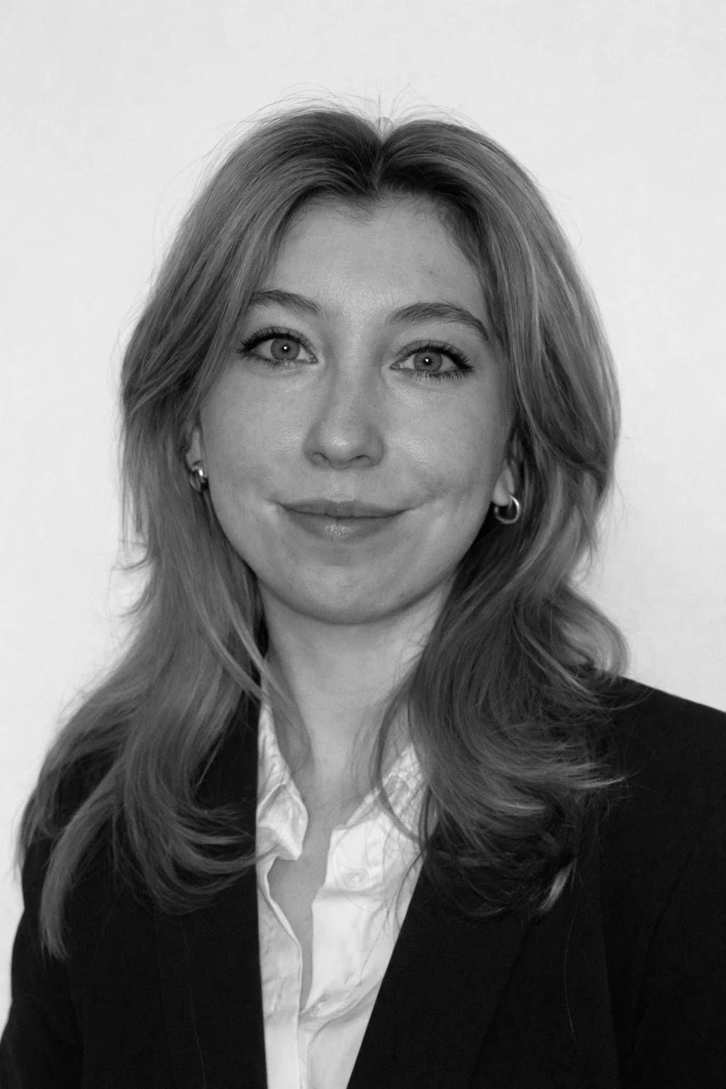 Black and white portrait of a woman (Callie Patten) with shoulder-length wavy hair, wearing earrings, a white shirt, and a dark blazer, smiling softly at the camera.