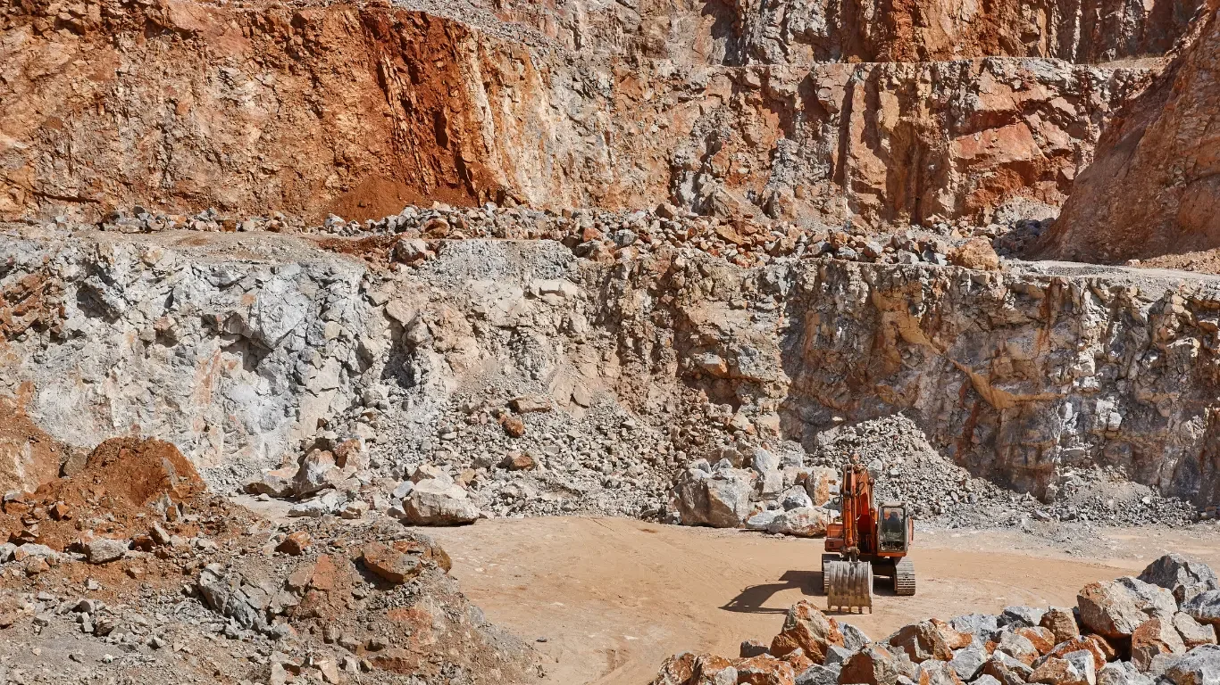 An orange excavator working in a rocky, mountainous excavation site.